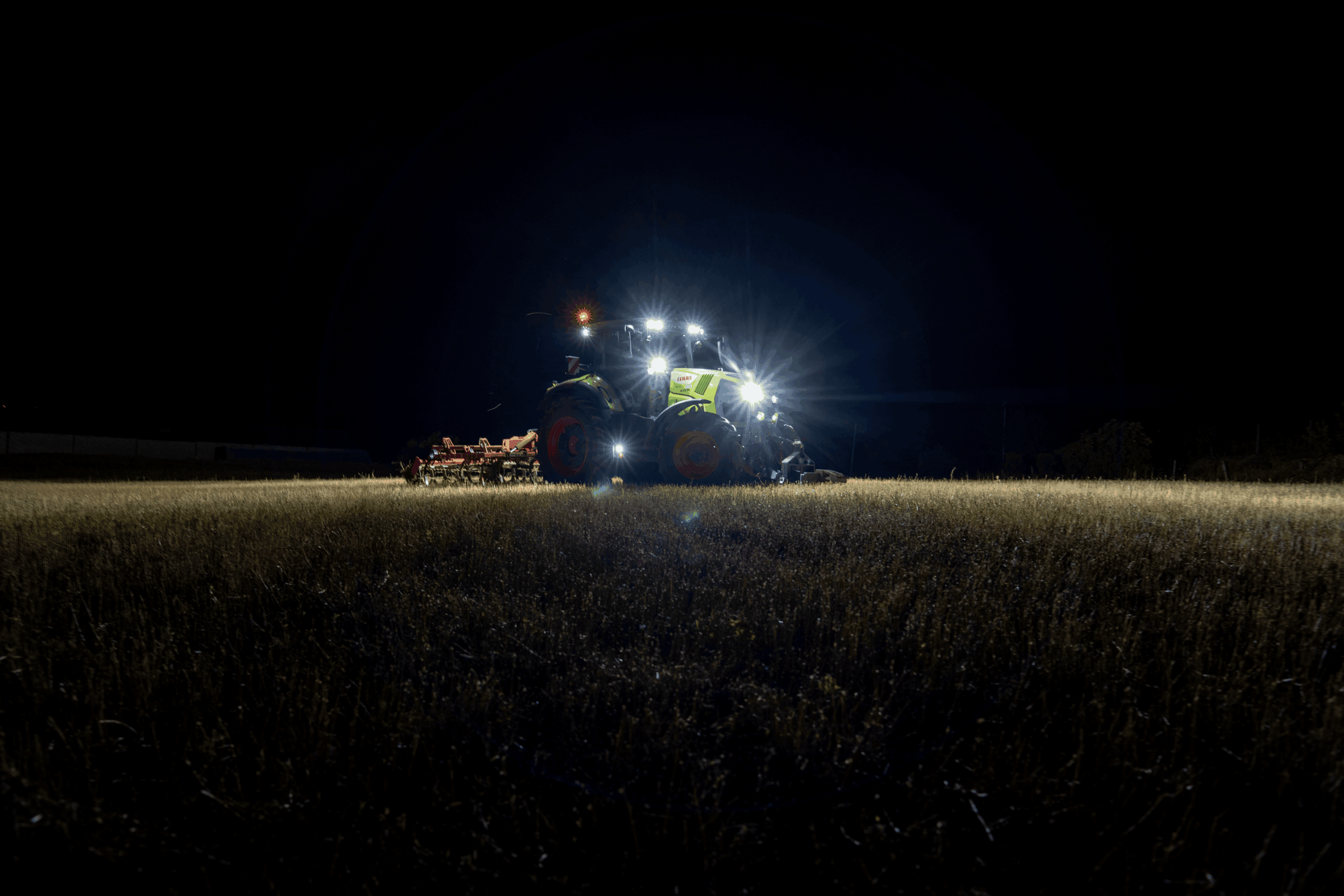 Trois tracteurs Fendt alignés sur un terrain non goudronné en pleine lumière du jour, avec paysage verdoyant en arrière-plan