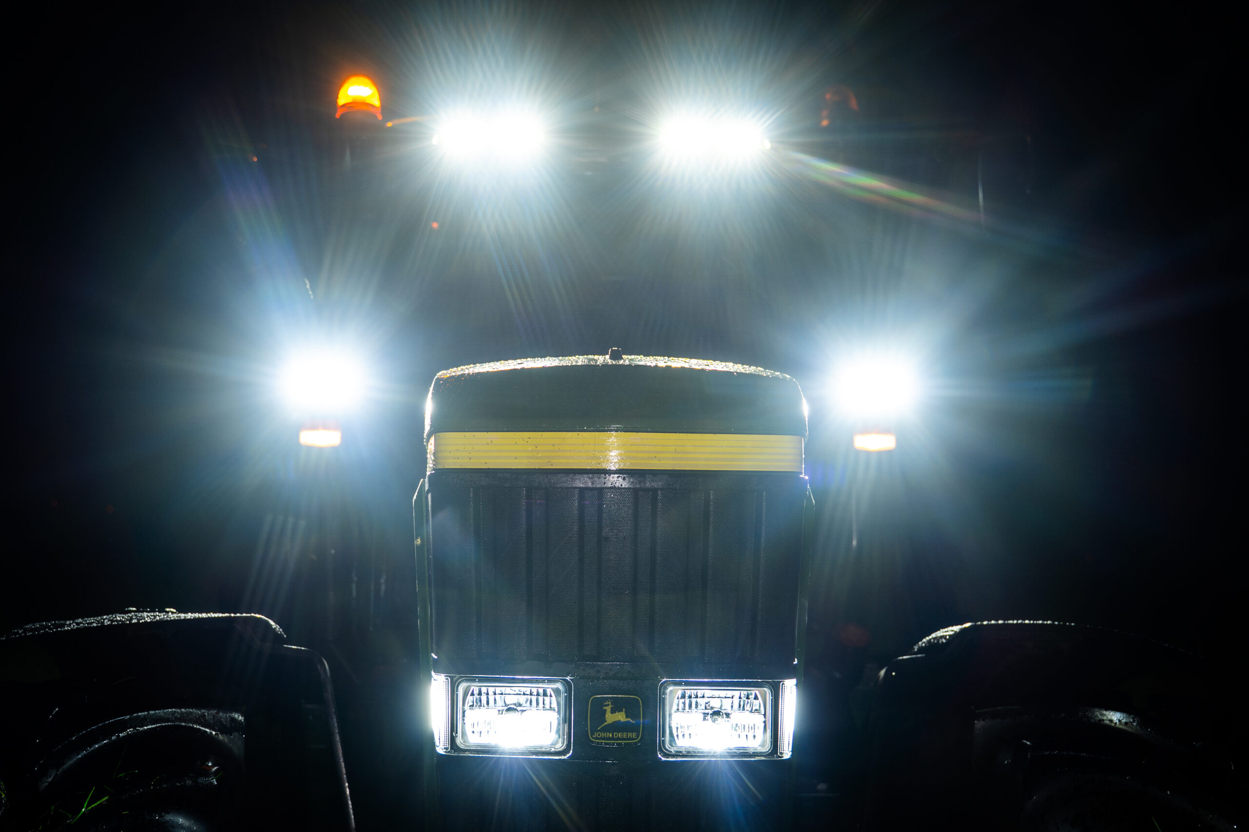 Tracteur John Deere de face la nuit, phares LED et gyrophares allumés.
