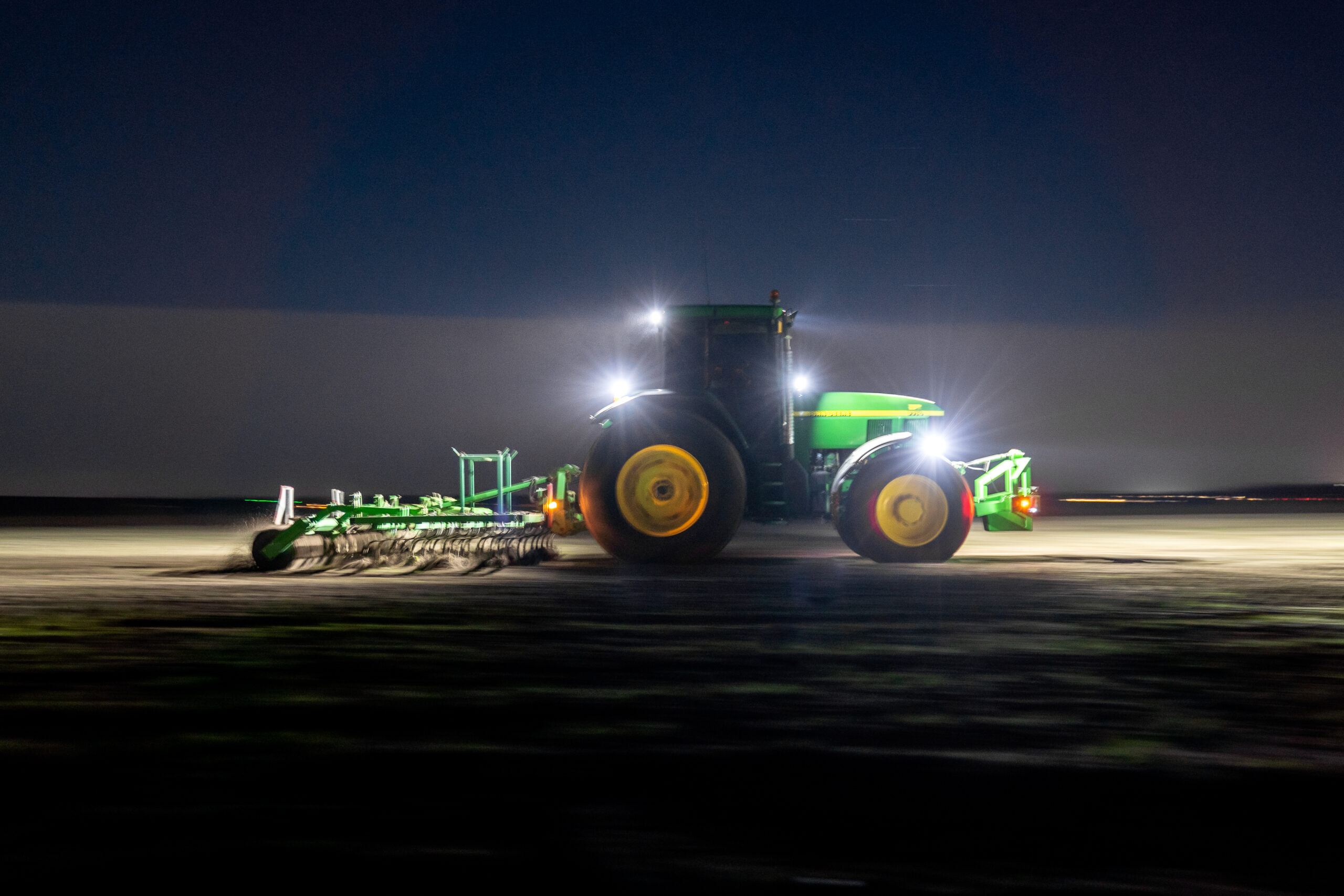 Tracteur agricole au travail de nuit dans un champ, éclairé par des phares LED puissants.