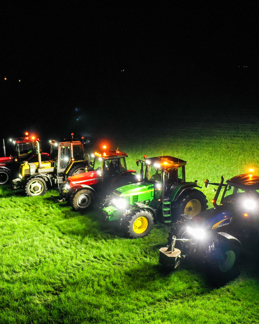 Tracteurs agricoles alignés de nuit dans un champ, phares et gyrophares allumés.